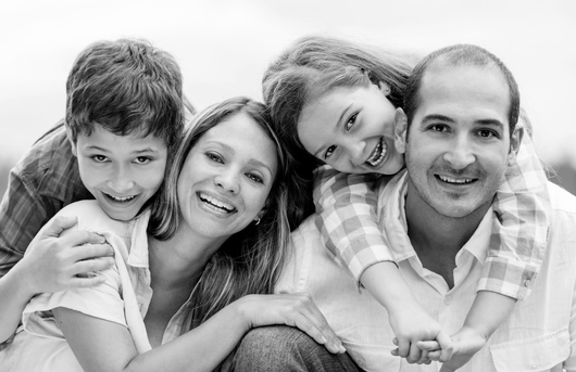 Une famille souriante de quatre personnes assises côte à côte sur un canapé, sur une photo en noir et blanc