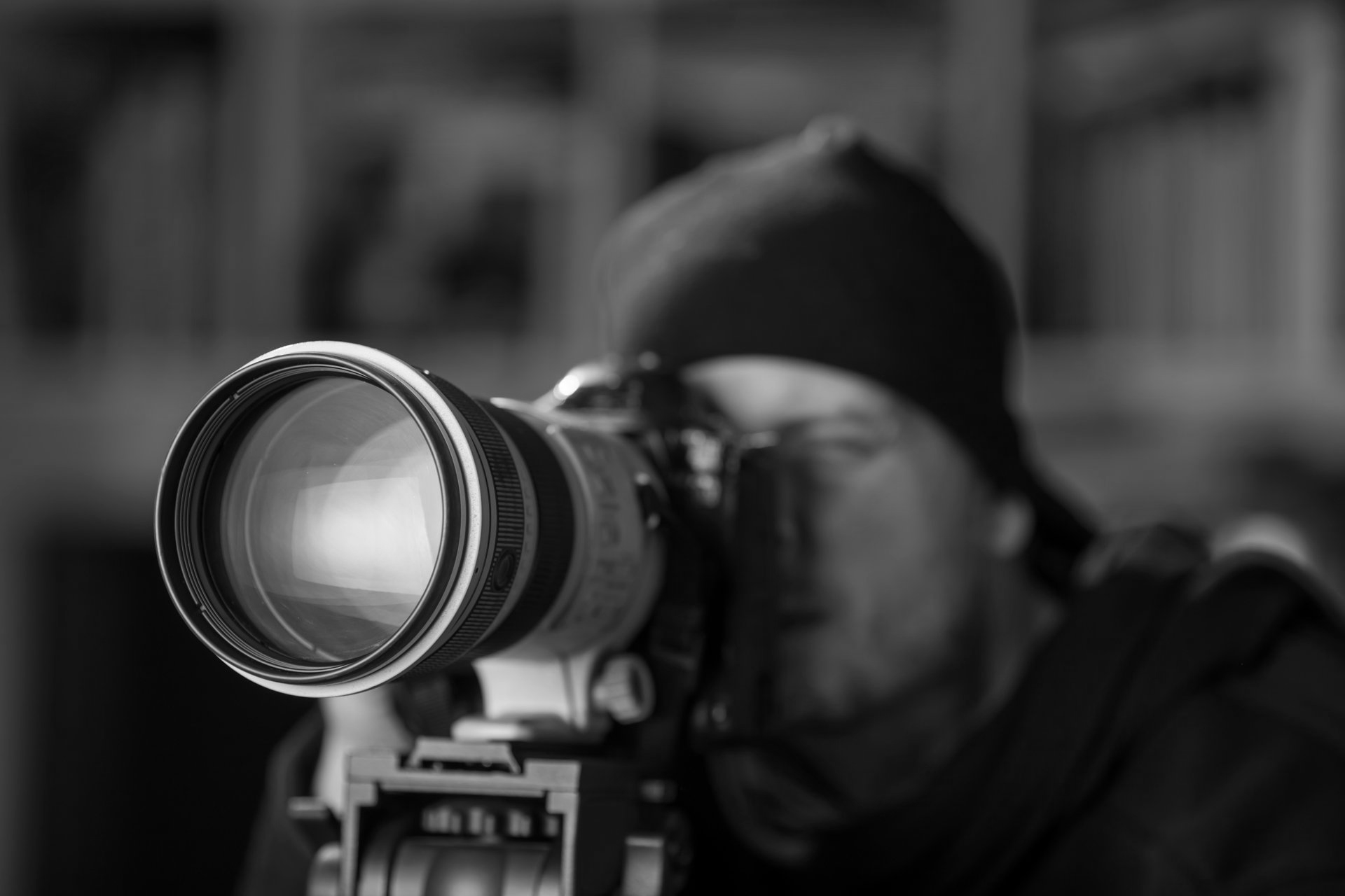 Un photographe pointe un appareil photo équipé d'un gros objectif dans un gros plan en noir et blanc.