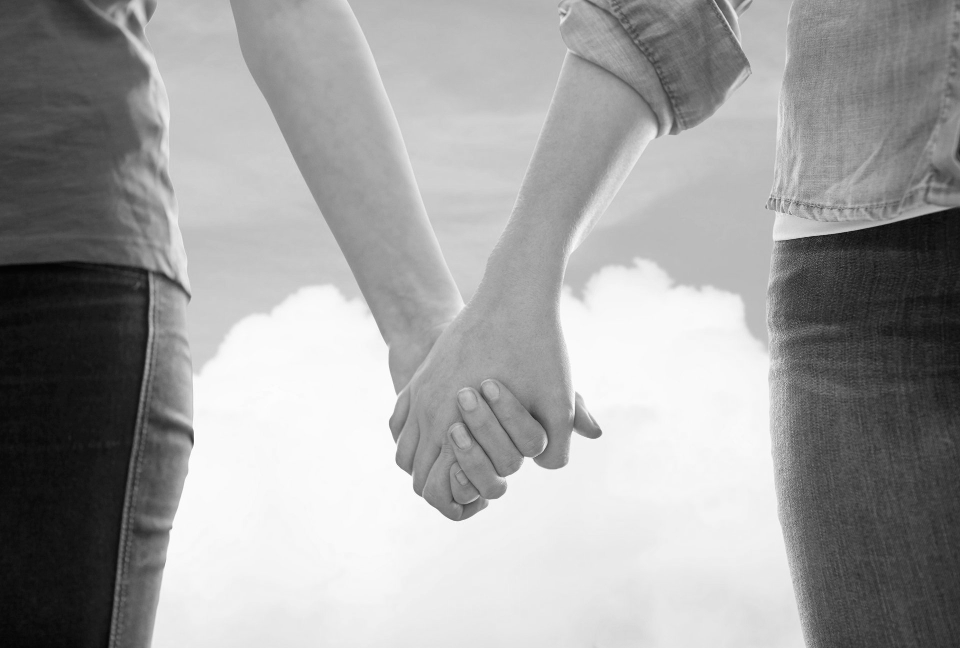 Deux personnes se tenant la main sur fond de ciel nuageux, photo en noir et blanc