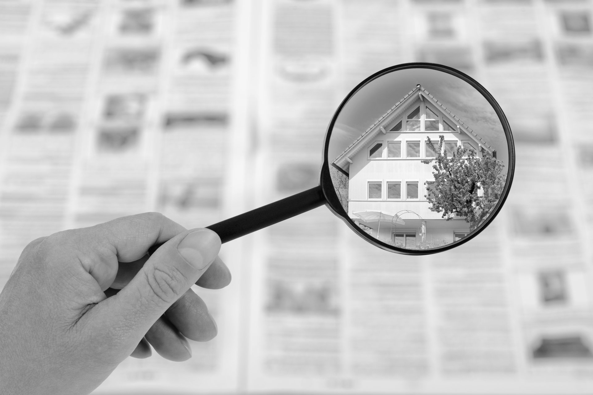 Main tenant une loupe au-dessus d'une maison sur fond de journal flou