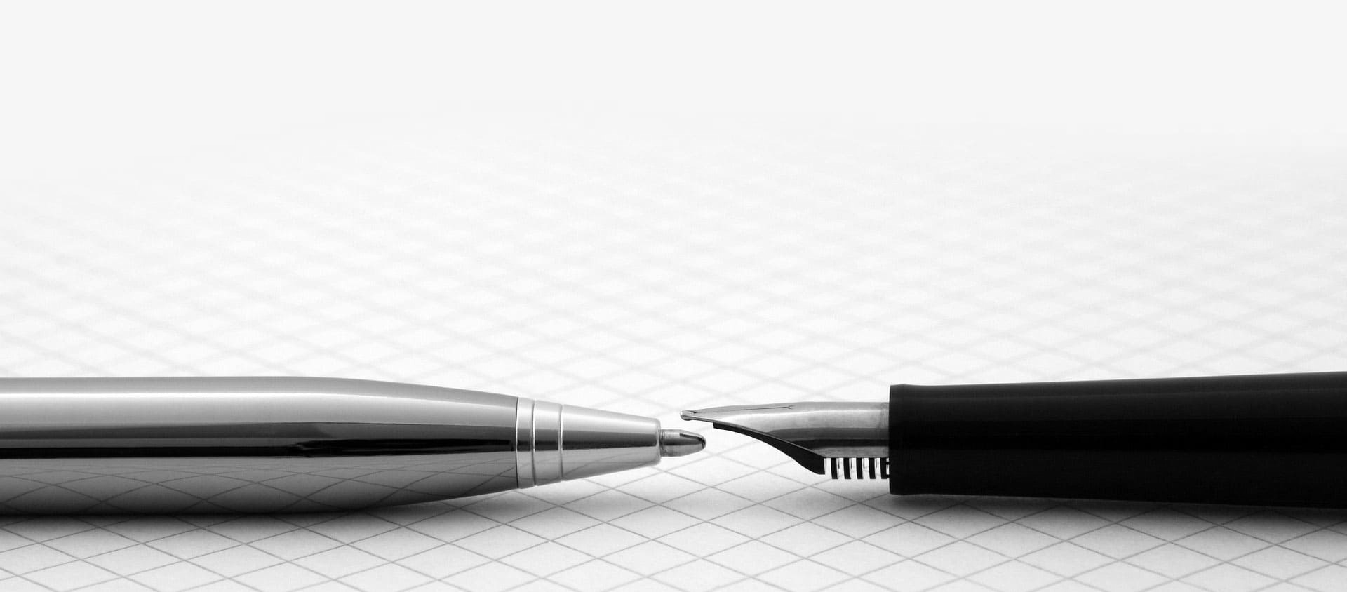 Deux pointes de stylo métalliques presque jointives, l'une argentée et l'autre noire, sur un fond quadrillé blanc.