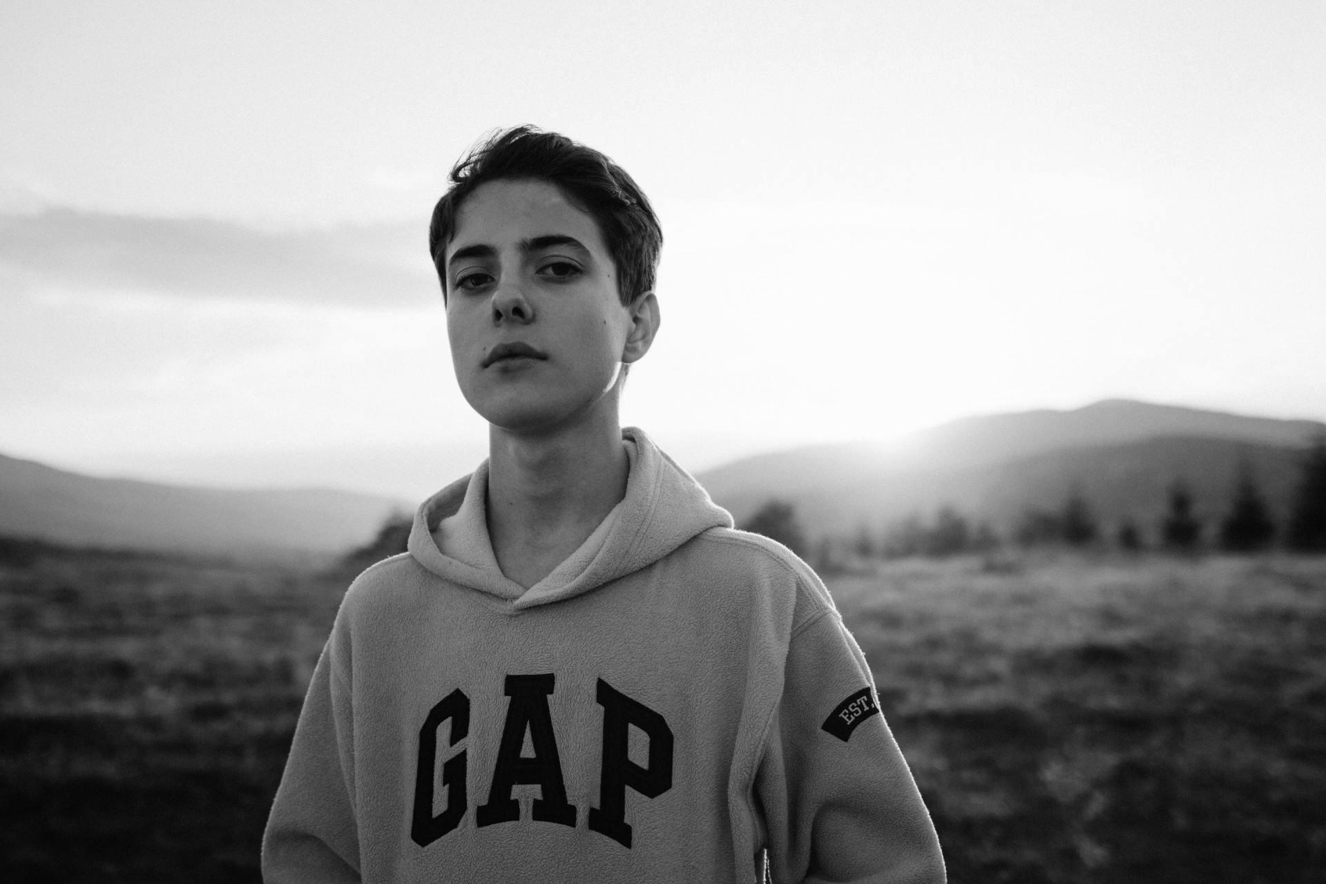 Une personne portant un sweat-shirt à capuche GAP se tient dans un champ avec des montagnes en arrière-plan.