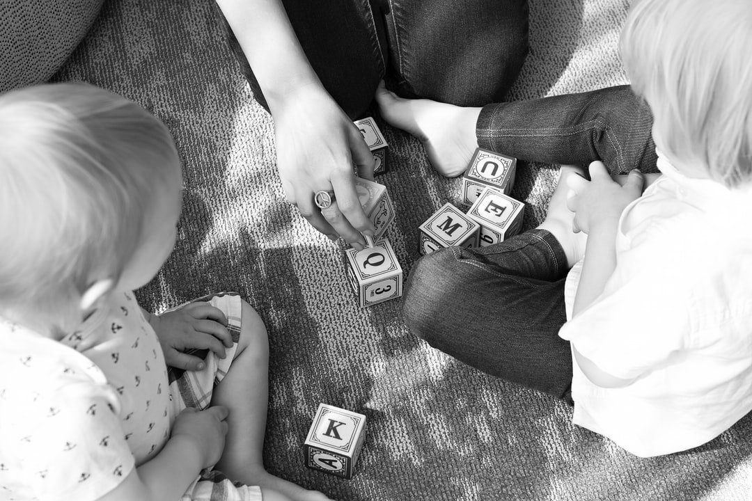 Trois enfants jouent avec des cubes de l'alphabet sur un sol recouvert de moquette.