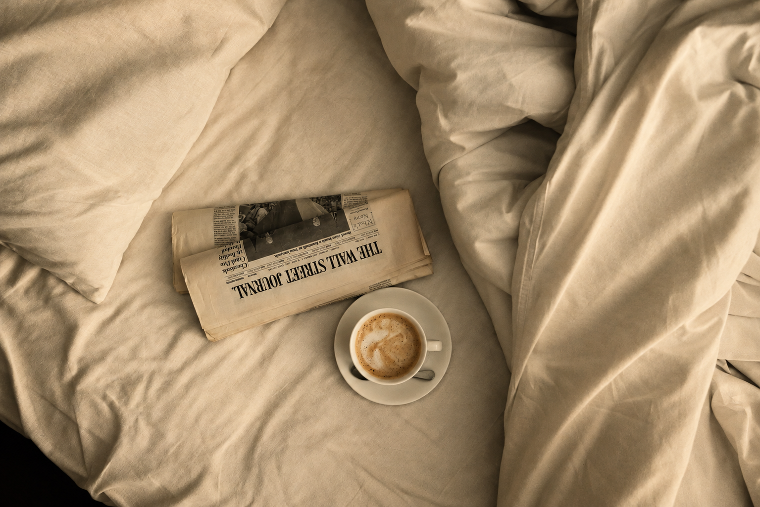 Kaffeetasse und Zeitung auf zerknitterter beiger Bettwäsche – ein gemütlicher Morgen im Bett