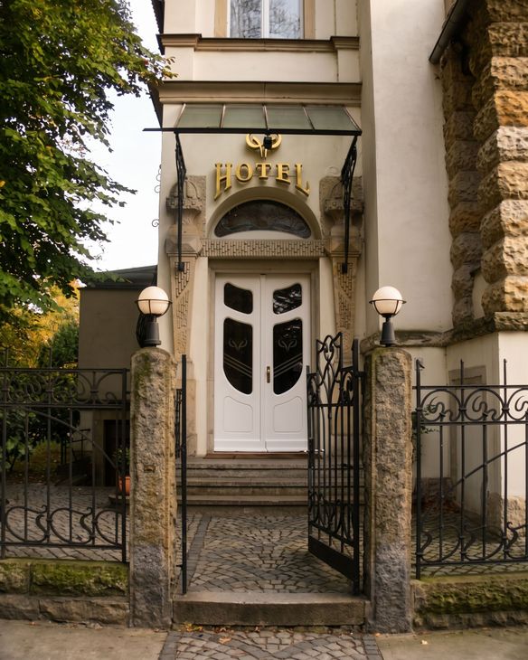 Eingang eines Hotels mit weißen Doppeltüren, Steinsäulen und einem schmiedeeisernen Tor