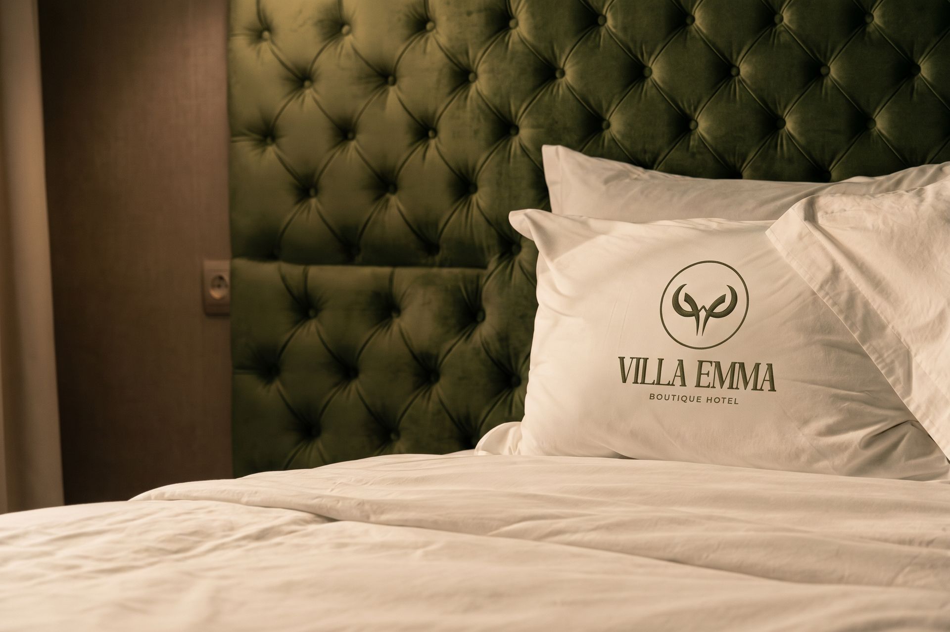 Kingsize-Bett mit weißer Bettwäsche und grünem, gepolstertem Kopfteil in einem Hotelzimmer