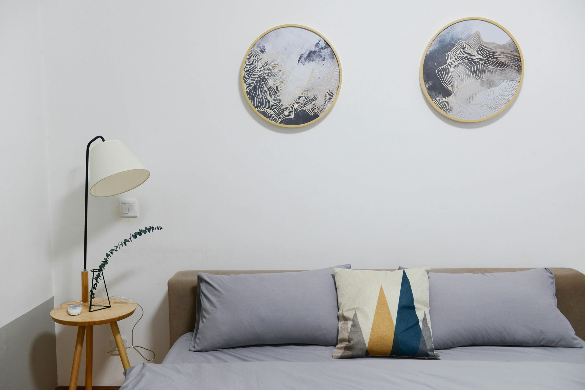 Minimalistisches Schlafzimmer mit Bett, Stehlampe, Nachttisch und zwei runden Wandbildern
