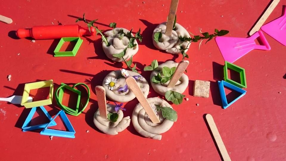 Tonfiguren, verziert mit Blättern und Blumen auf rotem Grund, umgeben von Kunststoff-Ausstechformen und Holzstäbchen.