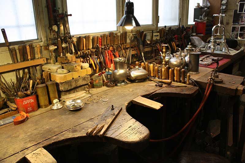 Atelier avec outils accrochés au mur, établi avec objets, petites fenêtres.