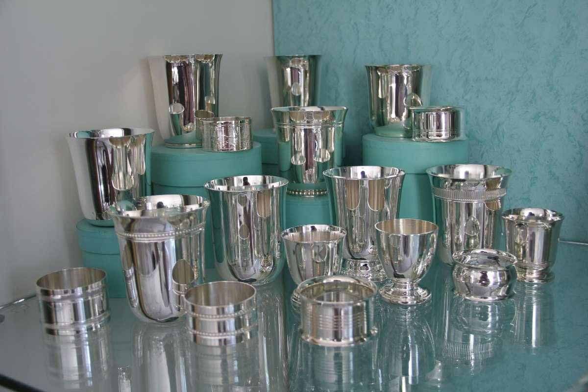 Collection d'argenterie : diverses tasses et gobelets disposés sur des socles turquoise et une étagère en verre.