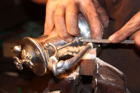 Des mains limant un objet en argent fixé dans un étau.