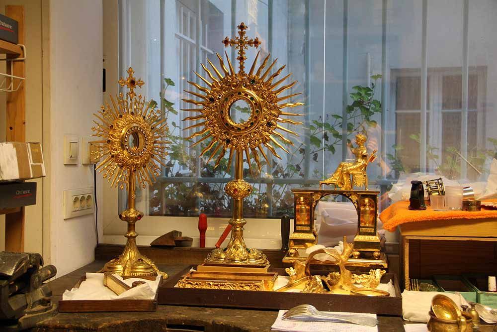 Deux ostensoirs en or richement décorés, contenant une petite statue en or, sont posés sur une table devant une fenêtre.