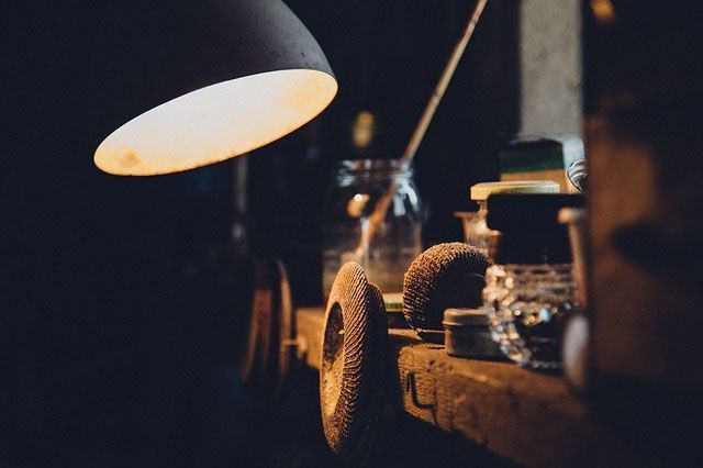 Un établi éclairé par une lampe ; divers objets, dont des bocaux en verre, une meuleuse en métal et des outils.