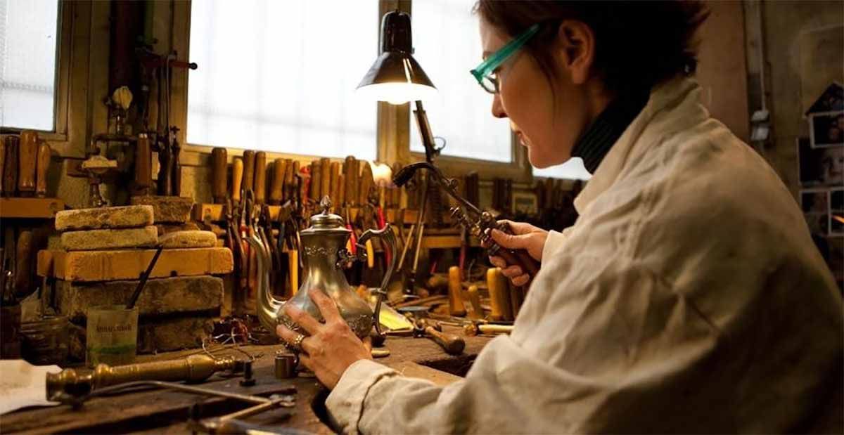 Femme en blouse blanche effectuant une soudure dans un atelier ; outils et lampe visibles.
