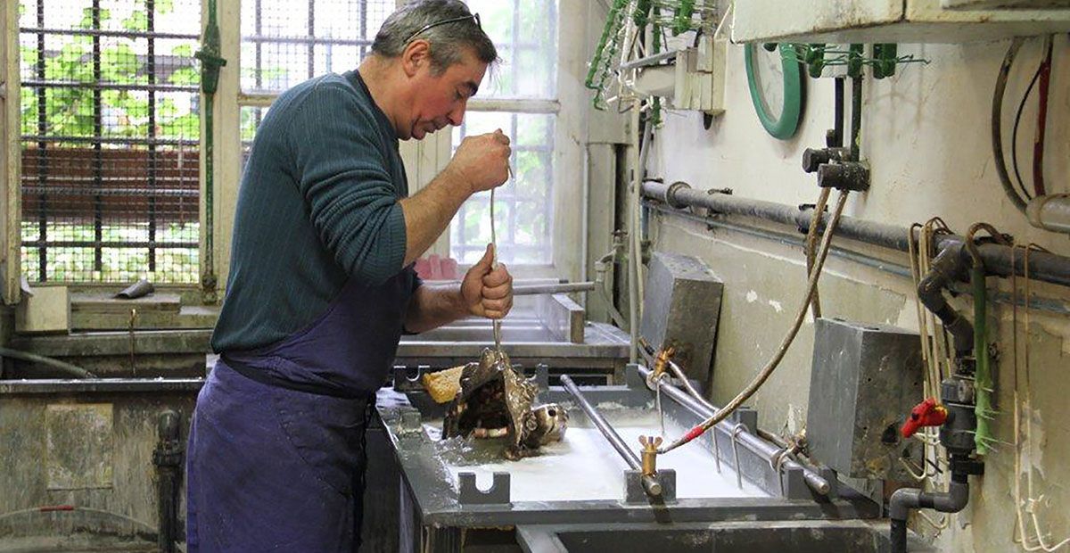 Un homme manipule du matériel dans un laboratoire. Il porte un tablier bleu et tient un outil au-dessus d'un récipient contenant des produits chimiques.