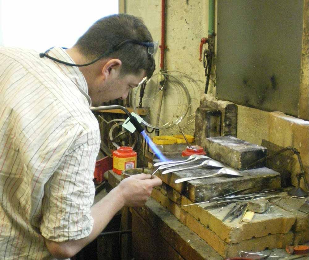 Un homme utilise une torche pour travailler des objets métalliques dans un atelier, en se concentrant sur la flamme.