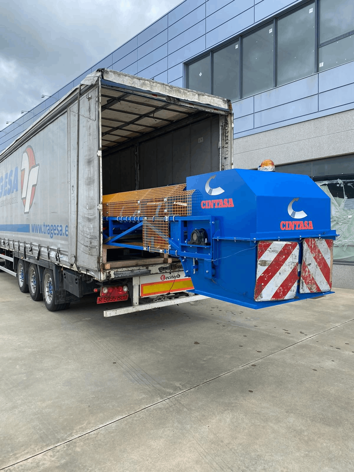 Un camión semirremolque azul y blanco está estacionado frente a un edificio.