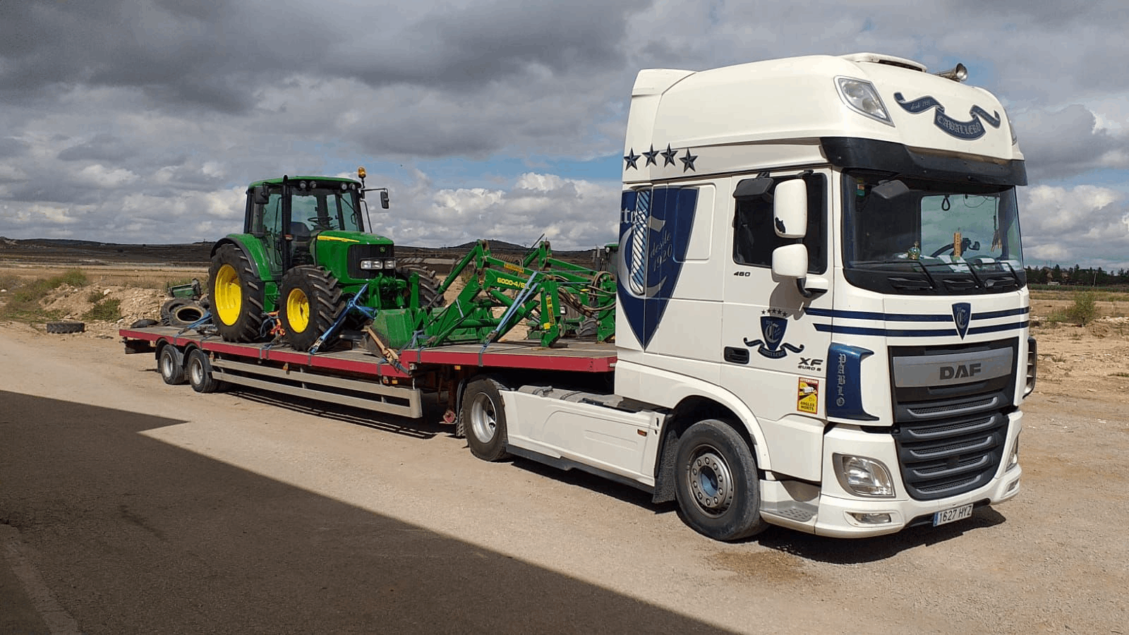 Un camión semirremolque blanco transporta un tractor verde en un remolque.