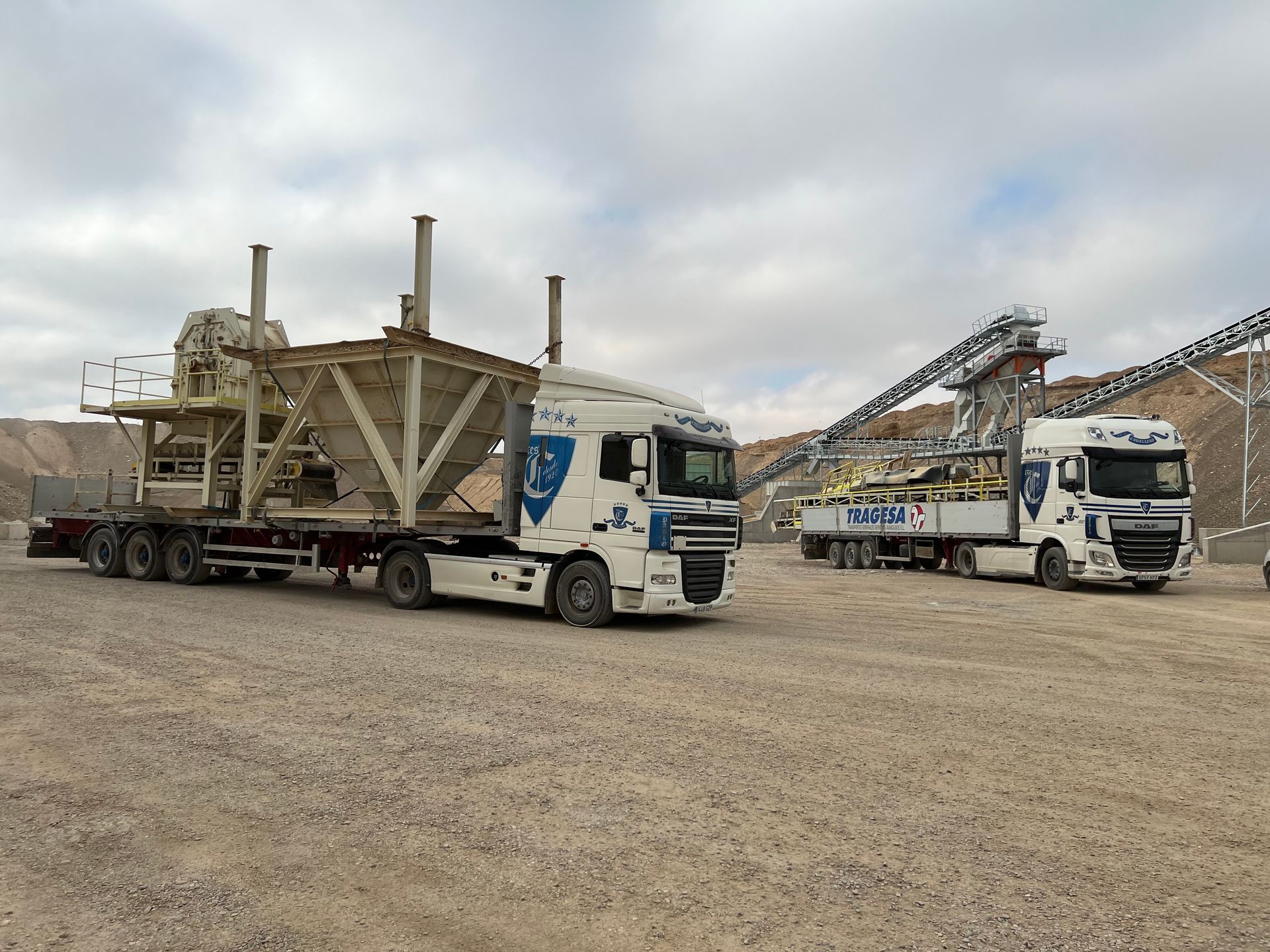 Dos camiones blancos están estacionados en un lote de grava.