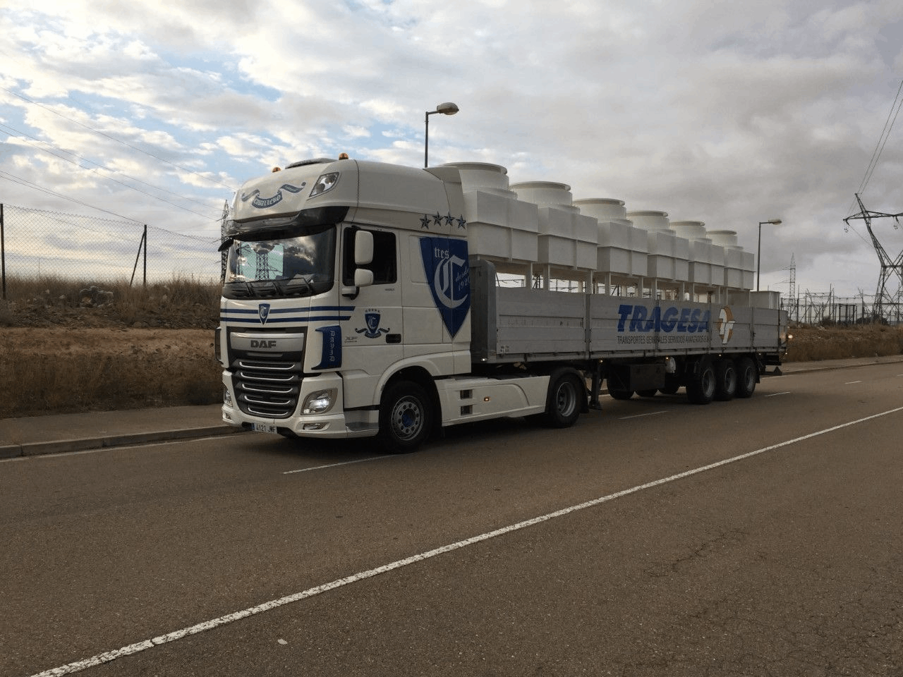 Un camión blanco circula por una carretera con un remolque lleno de tubos blancos.