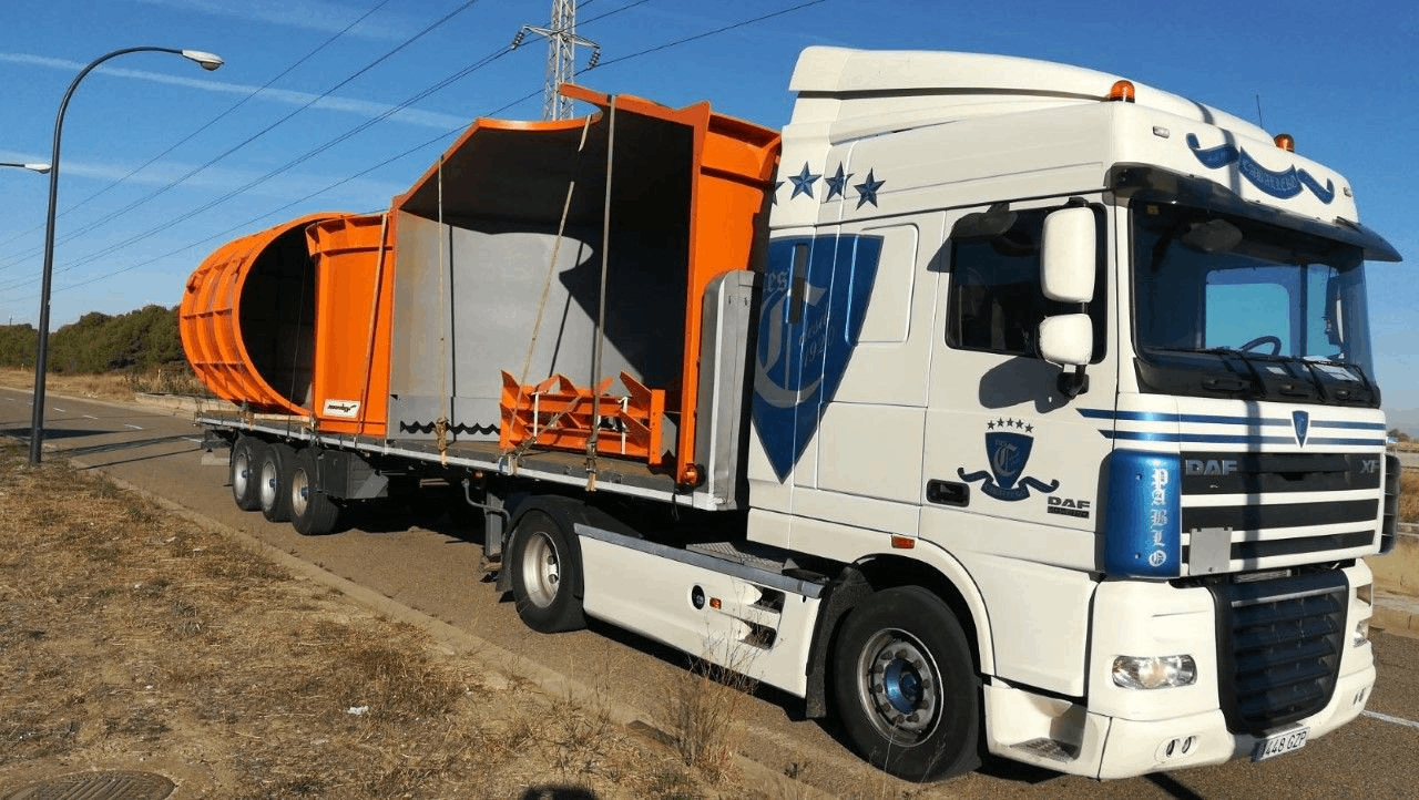 Un camión blanco transporta un gran contenedor naranja en un remolque.