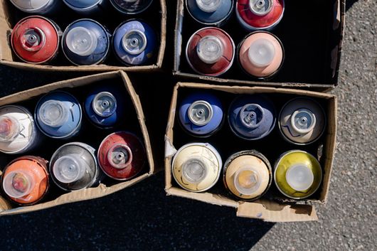 Un montón de latas de pintura en aerosol en cajas en el suelo