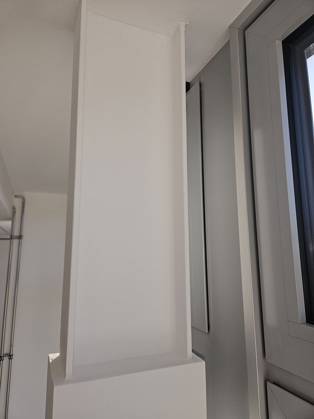 Eine weiße Säule in einem Raum neben einem Fenster.