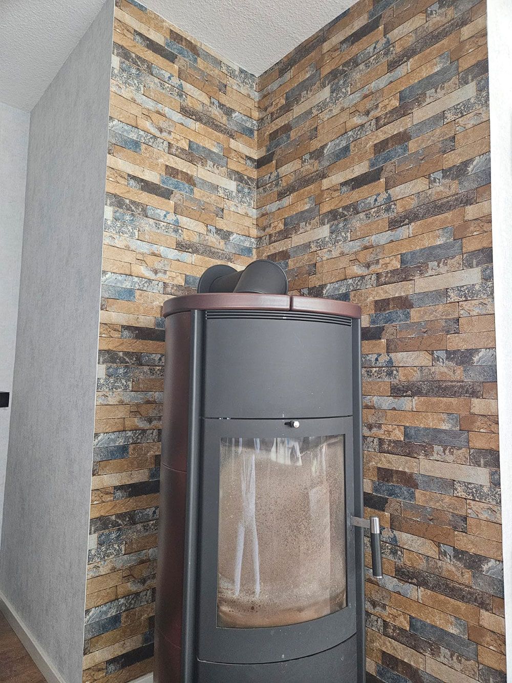 In einer Zimmerecke neben einer Backsteinwand steht ein Holzofen.