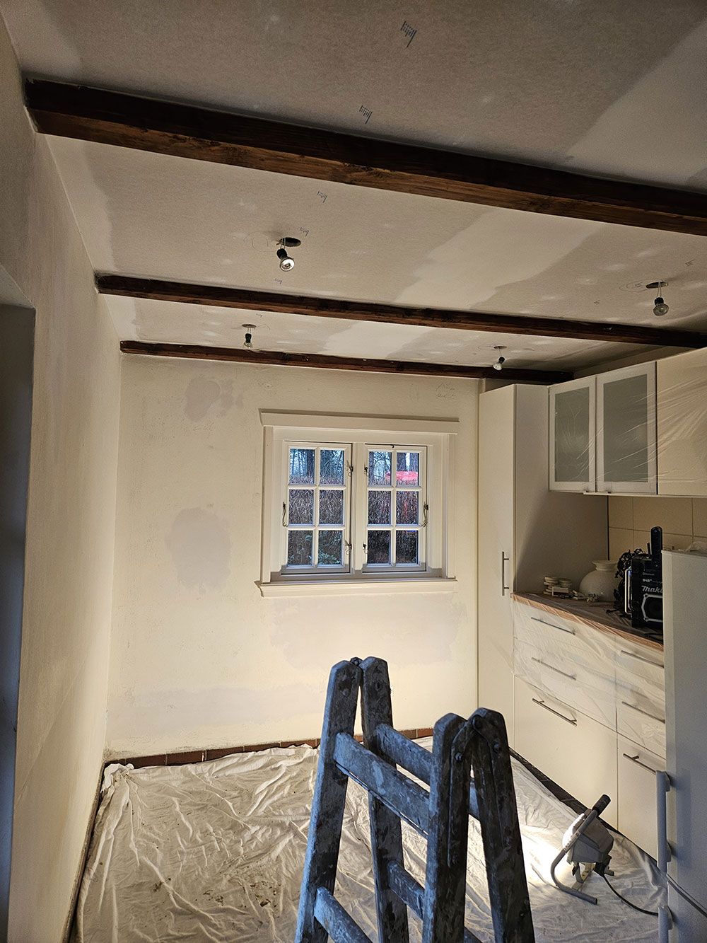 Eine Küche mit einer Leiter in der Mitte und einem Fenster.