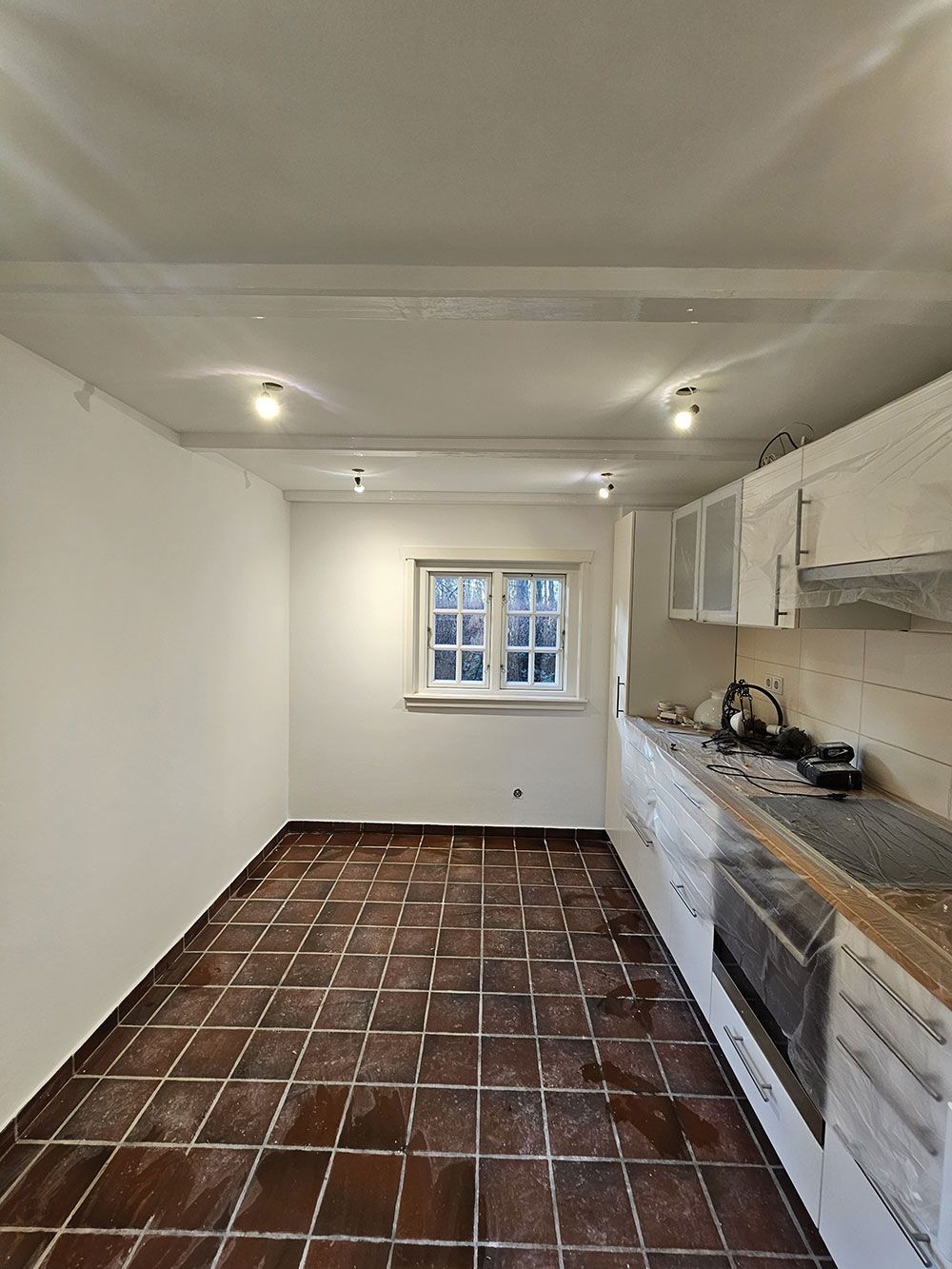 Eine leere Küche mit gefliestem Boden und weißen Schränken