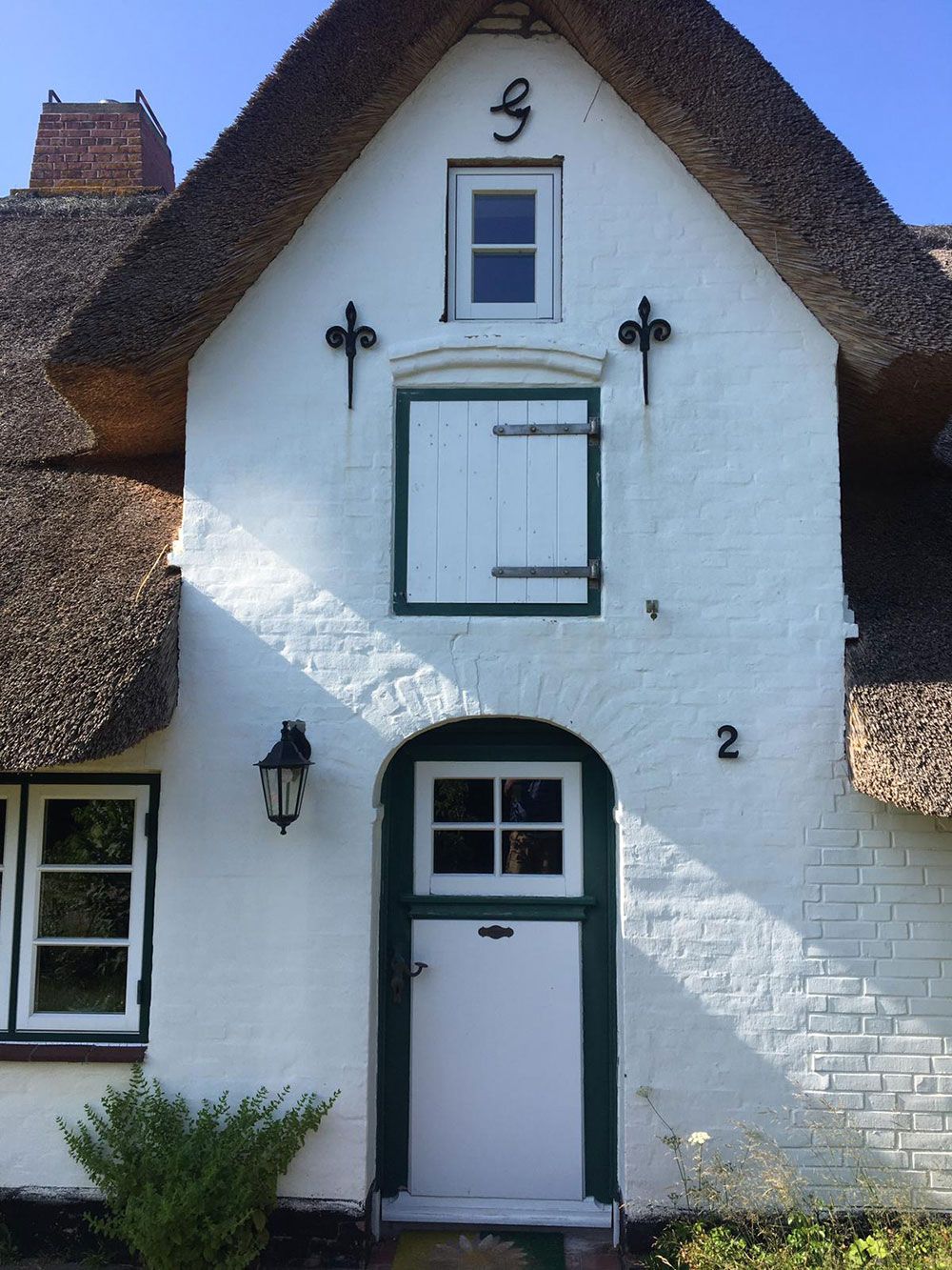 Ein weißes Haus mit Strohdach und der Nummer 2 darauf