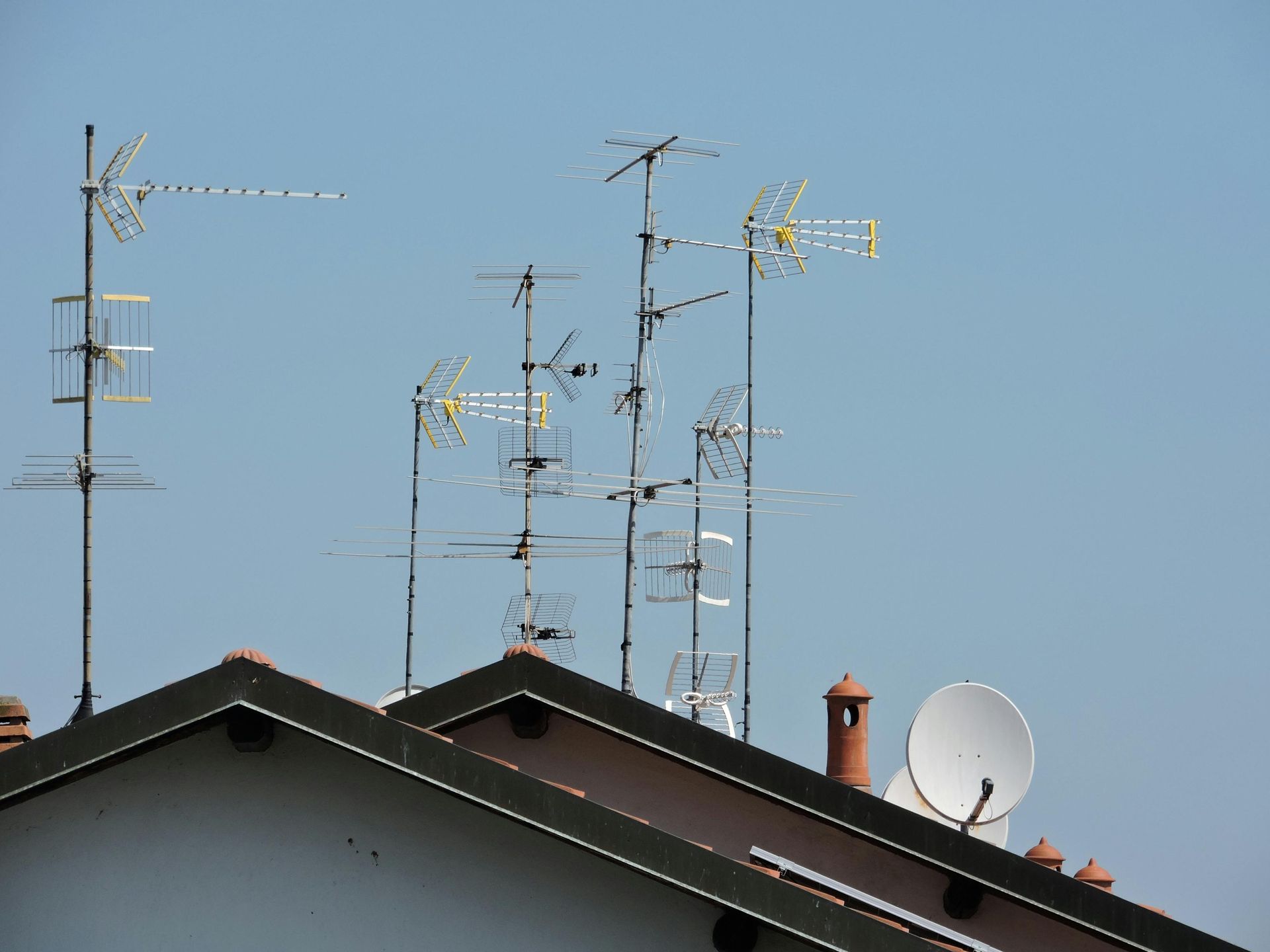 Azoteas con varias antenas de televisión y una antena parabólica blanca contra un cielo azul despejado.