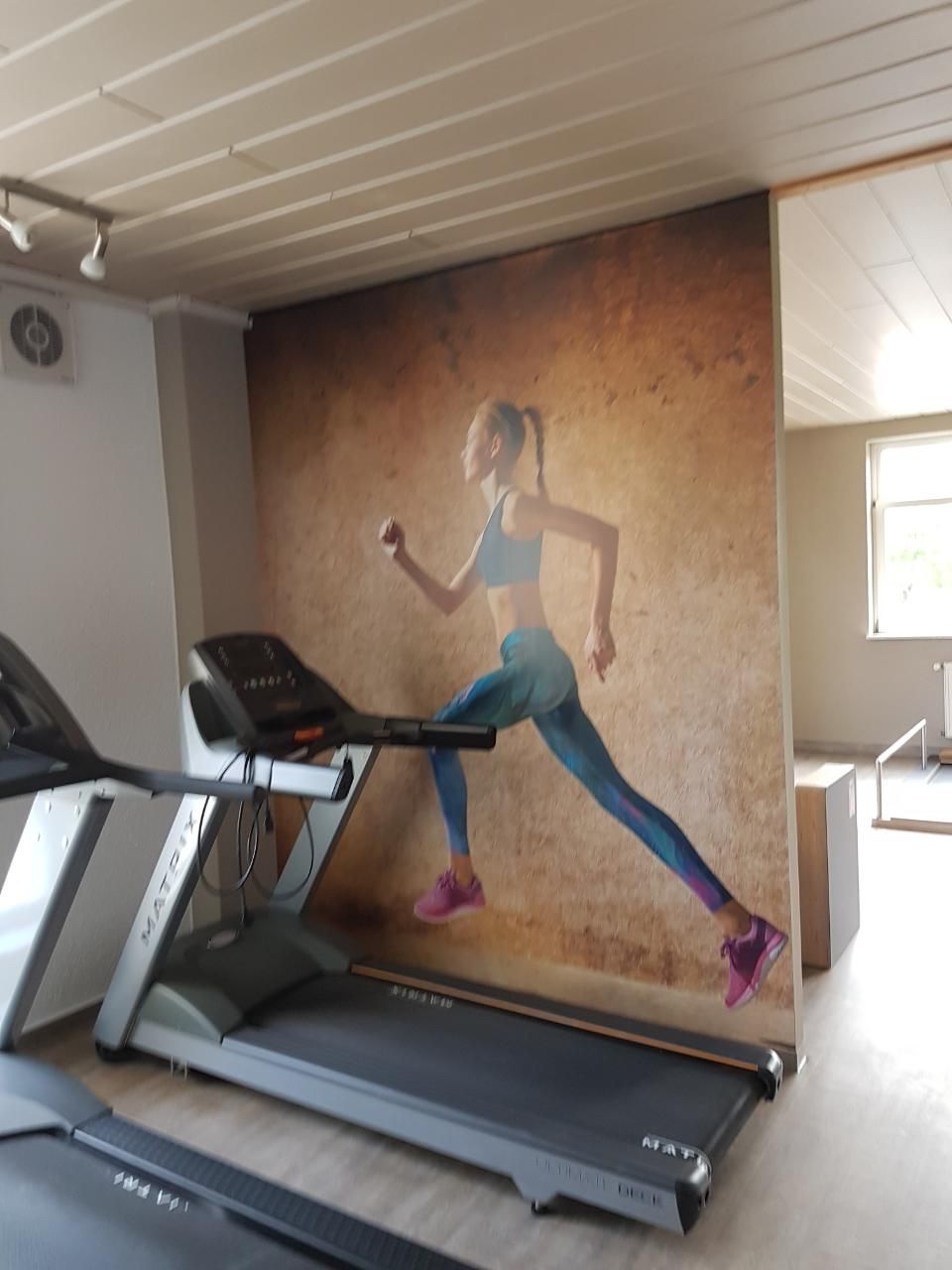 Malerbetrieb Blum GmbH & Co. KG, Tapete mit sportlicher Frau im Fitnessraum