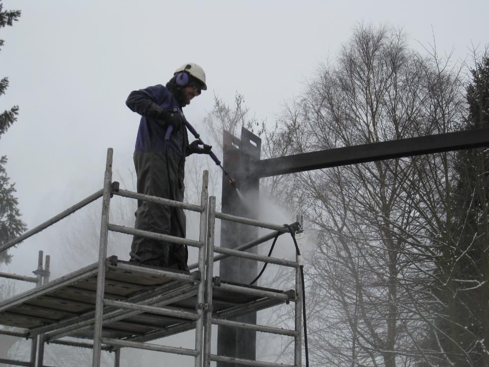 Malerbetrieb Blum GmbH & Co. KG, Mitarbeiter nimmt Hochdruckreinigungsarbeiten auf Gerüst vor