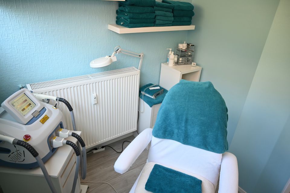 Kosmetikerzimmer: weißer Stuhl mit türkisfarbenem Handtuch, Lasergerät, türkisfarbene Handtücher auf Regalen.