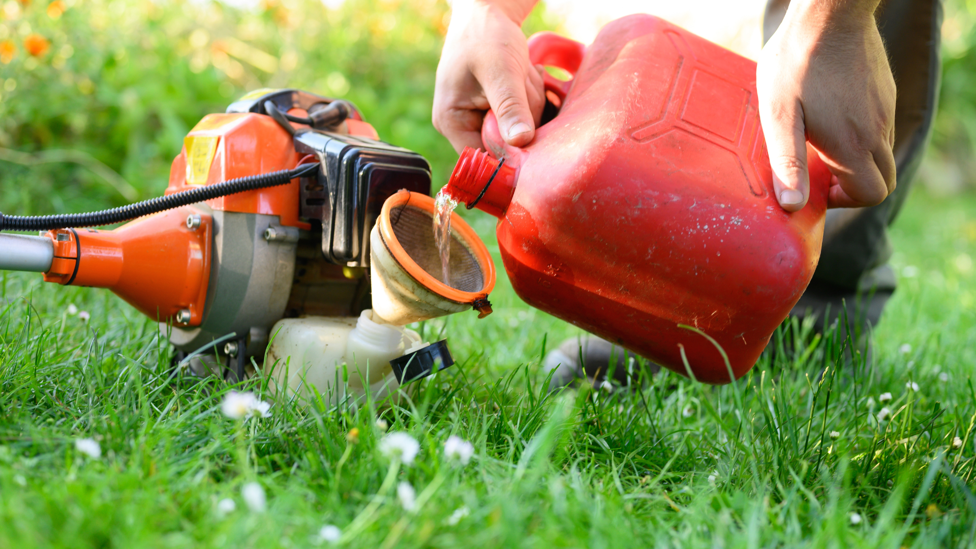 Une personne remplit le réservoir d'un coupe-bordures avec de l'essence provenant d'un bidon rouge dans une cour herbeuse.