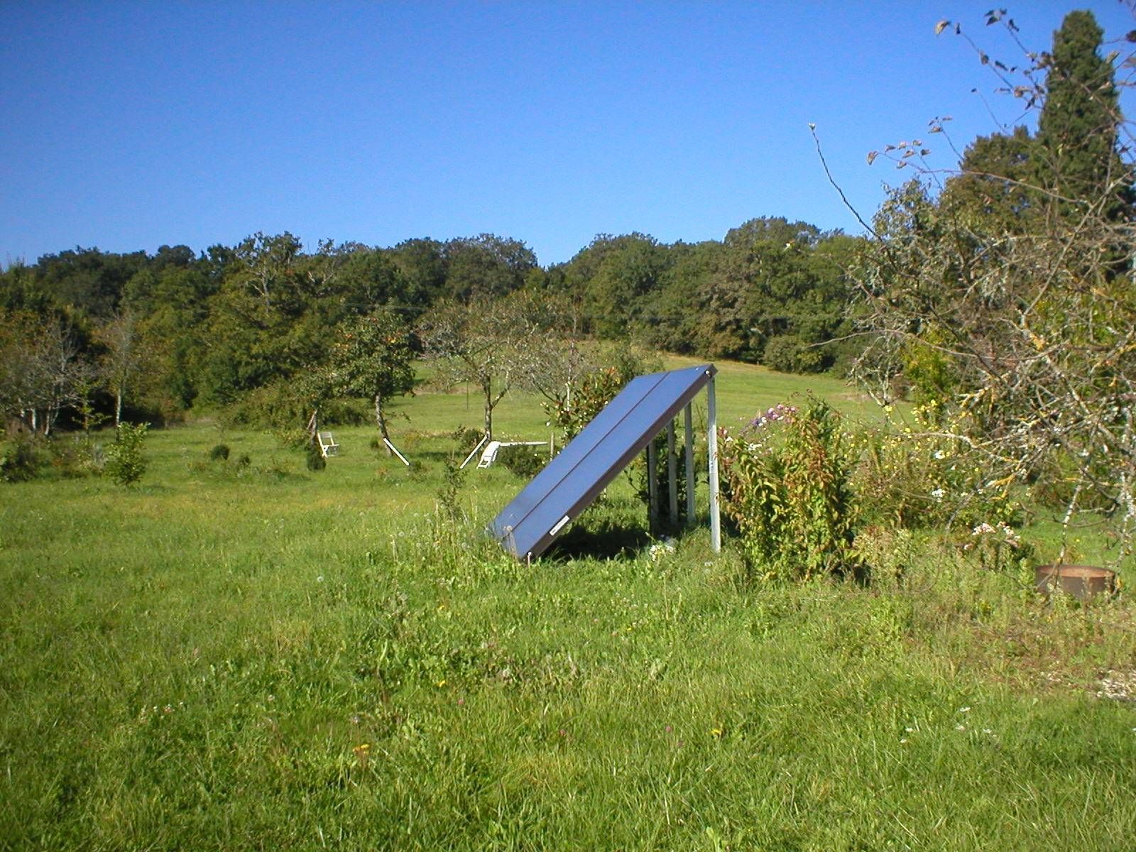 Panneau solaire dans un champ herbeux, avec des arbres sous un ciel bleu.
