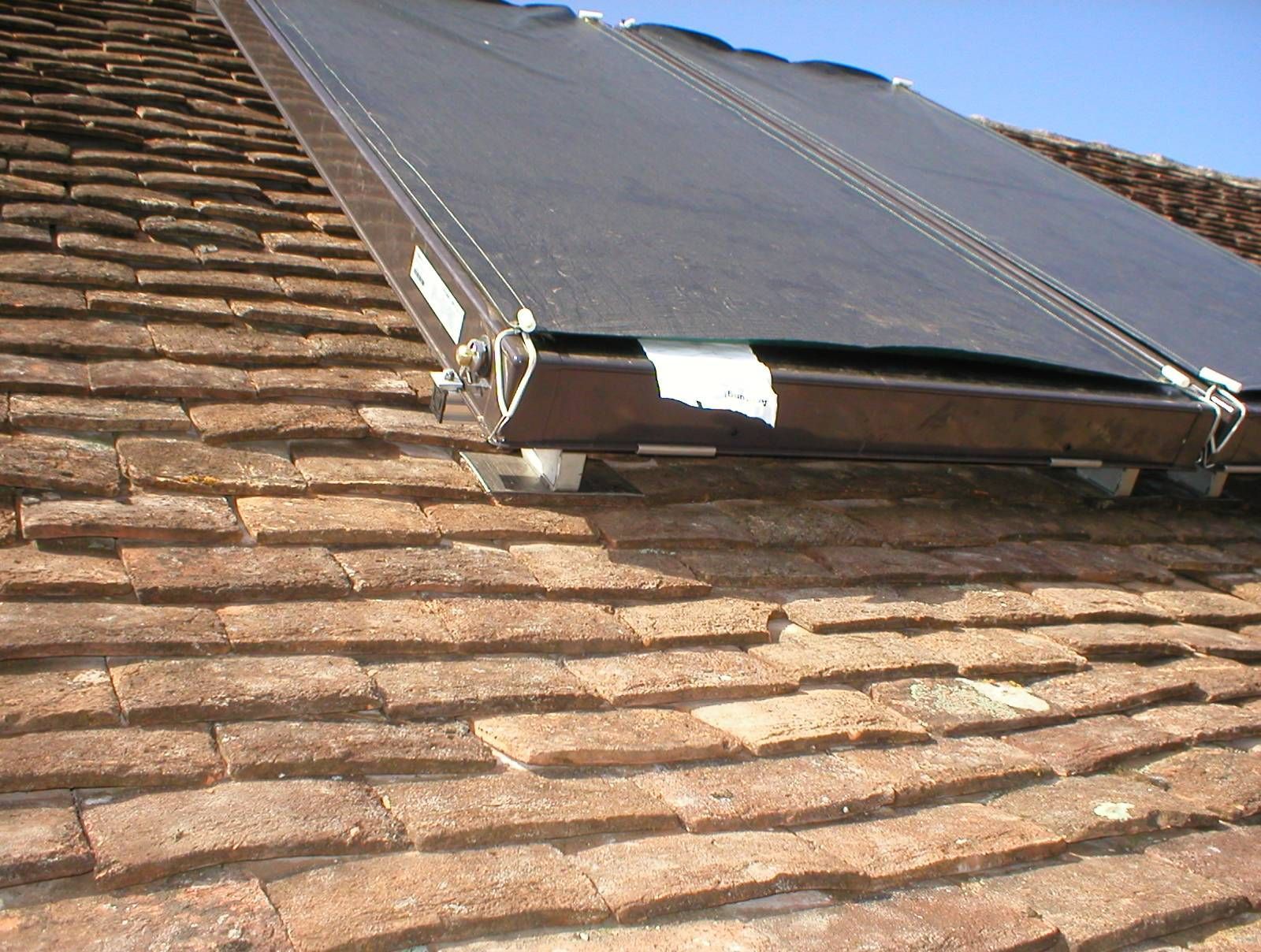 Panneau solaire installé sur un toit en tuiles sous un ciel bleu dégagé.