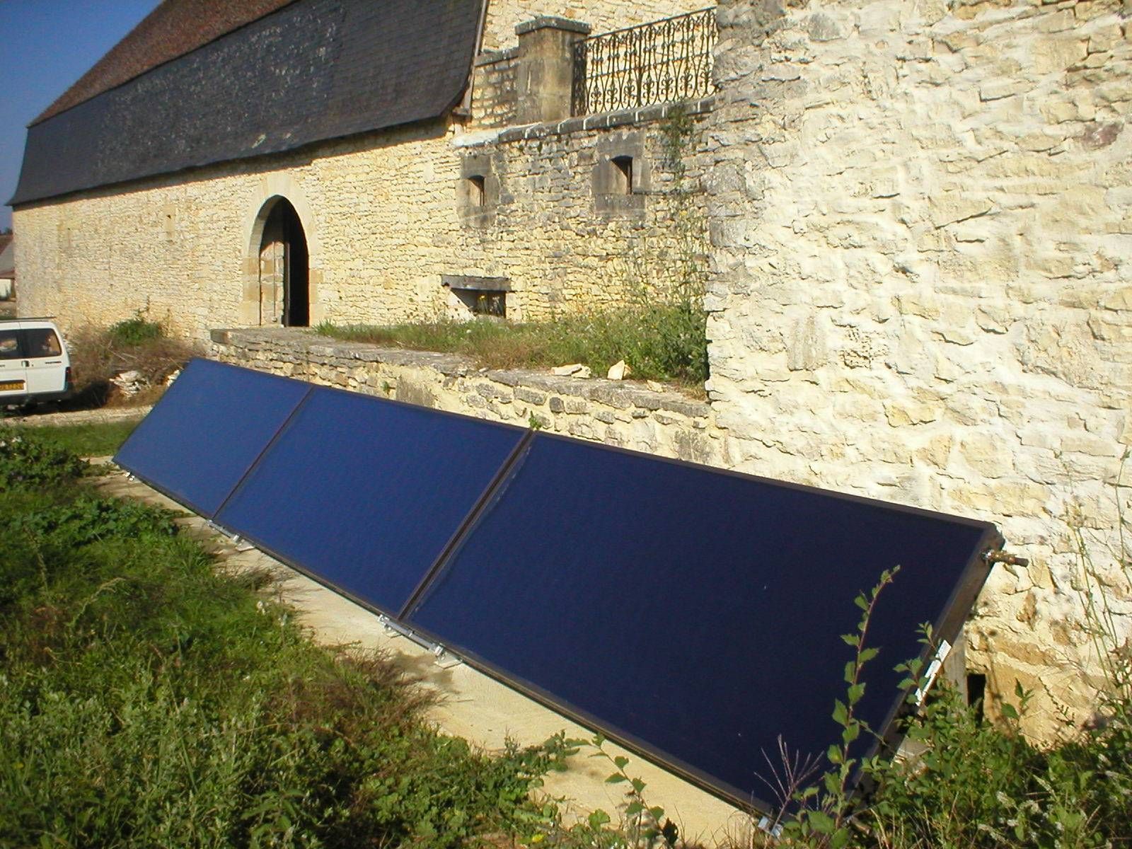 Des panneaux solaires bleus appuyés contre un bâtiment en pierre, dans une cour herbeuse