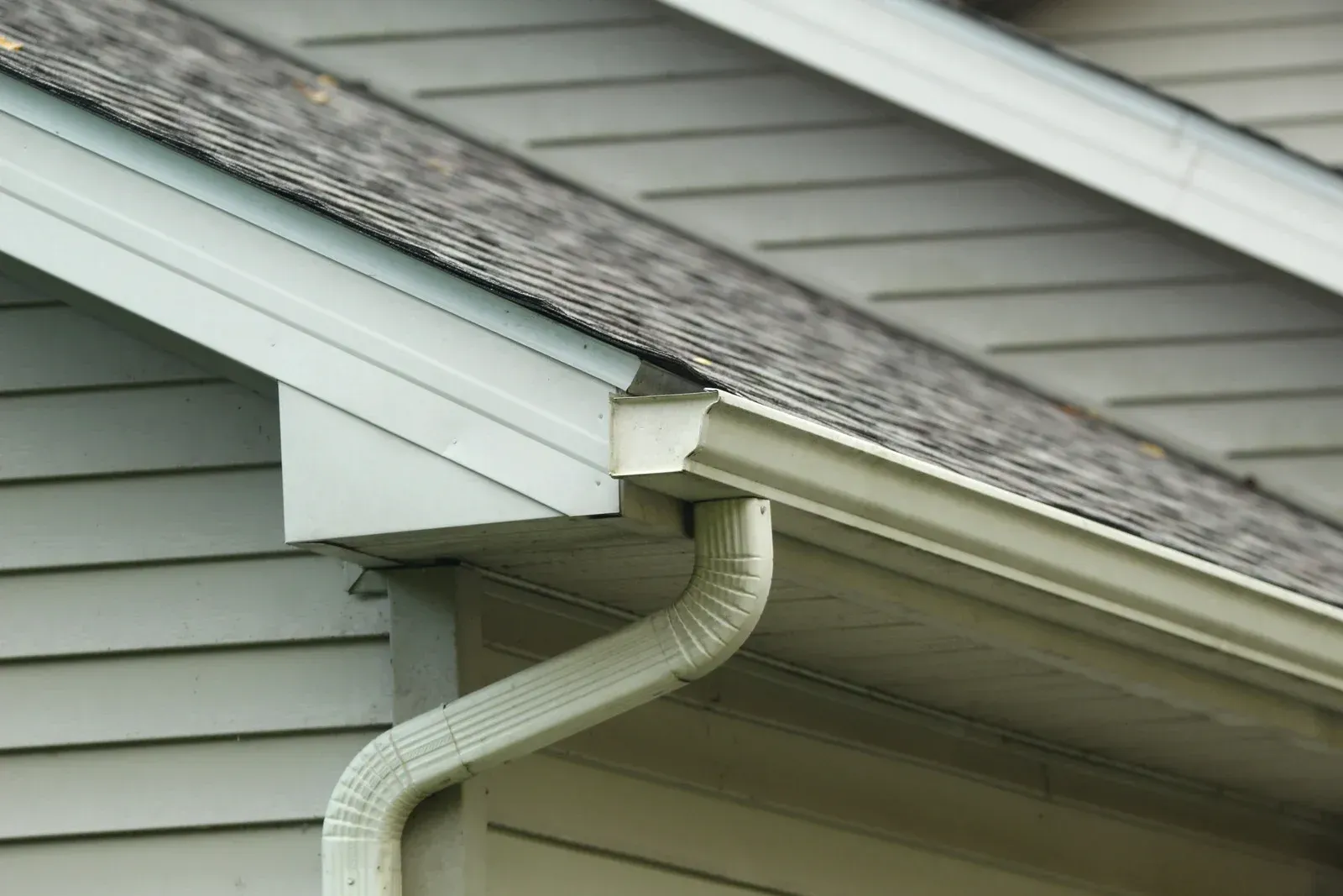 White gutter downspout attached to the corner of a gray house beneath the roofline