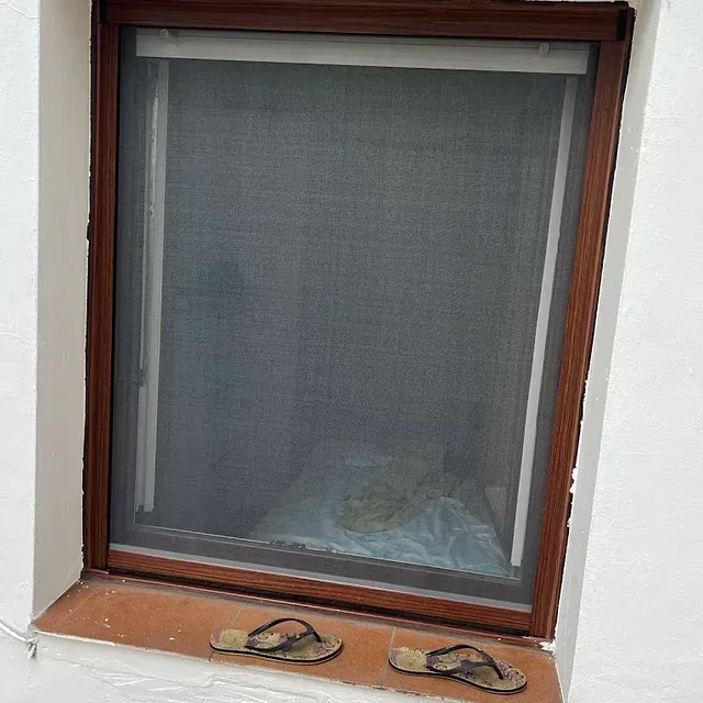 Un par de chanclas están en el alféizar de una ventana al lado de una ventana con mosquitera.