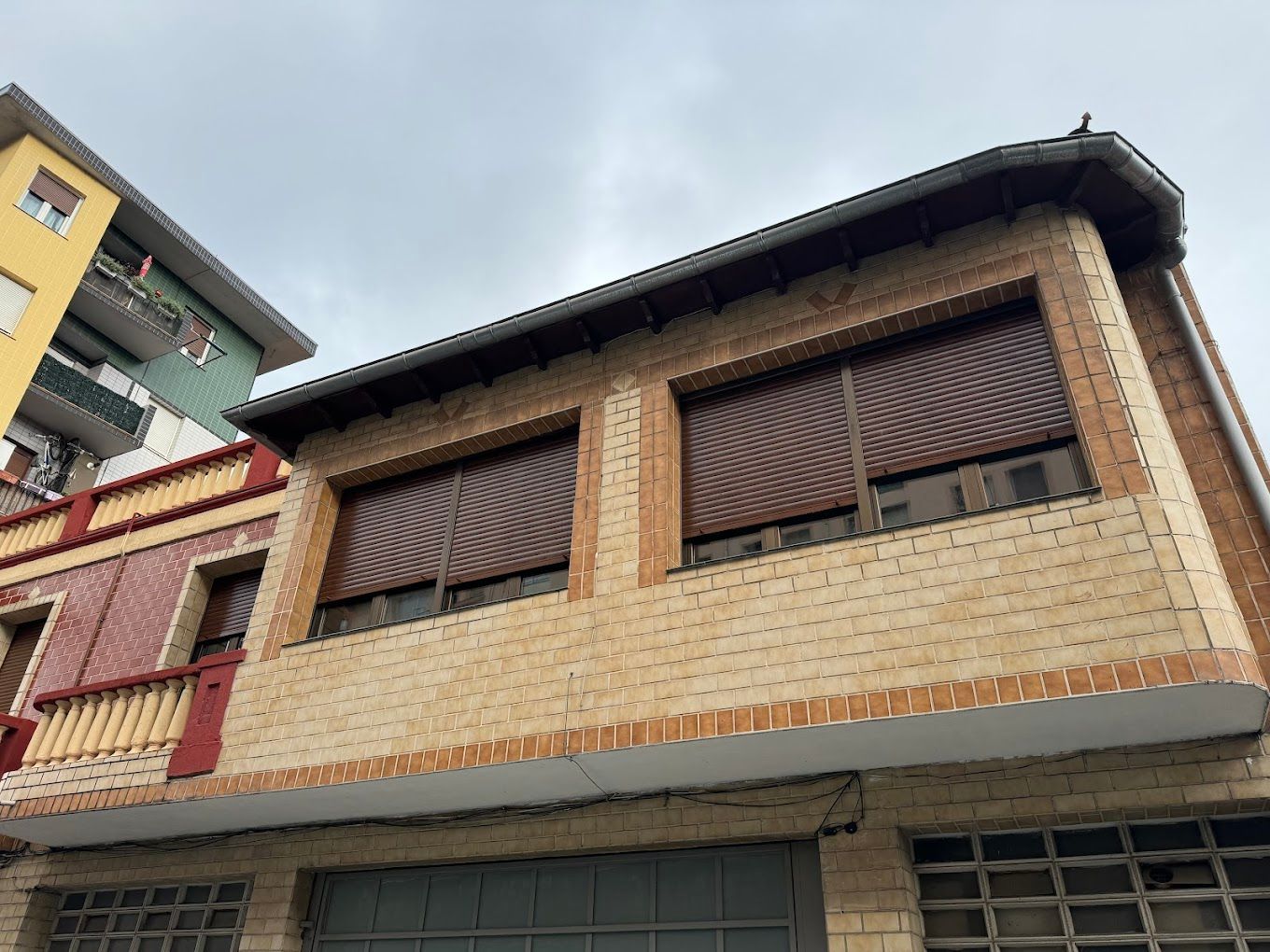Un edificio de ladrillo con persianas en las ventanas y un edificio amarillo al fondo.