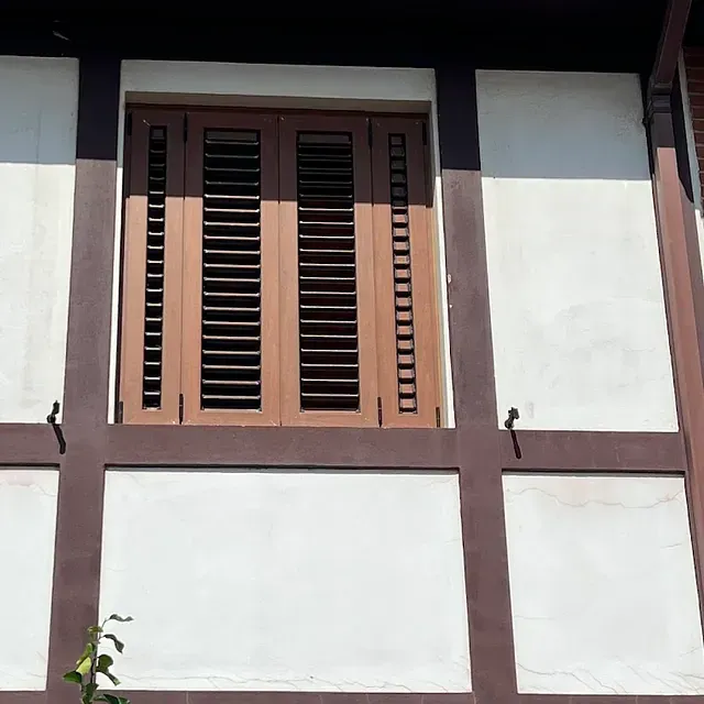 Una ventana con contraventanas de madera en un edificio blanco y marrón.