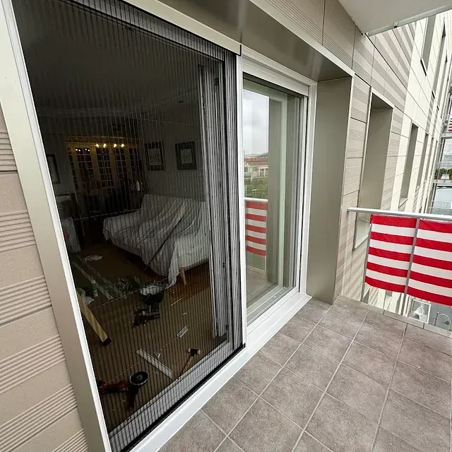 Una puerta corrediza de vidrio que conduce a un balcón con una bandera estadounidense colgando de la barandilla.