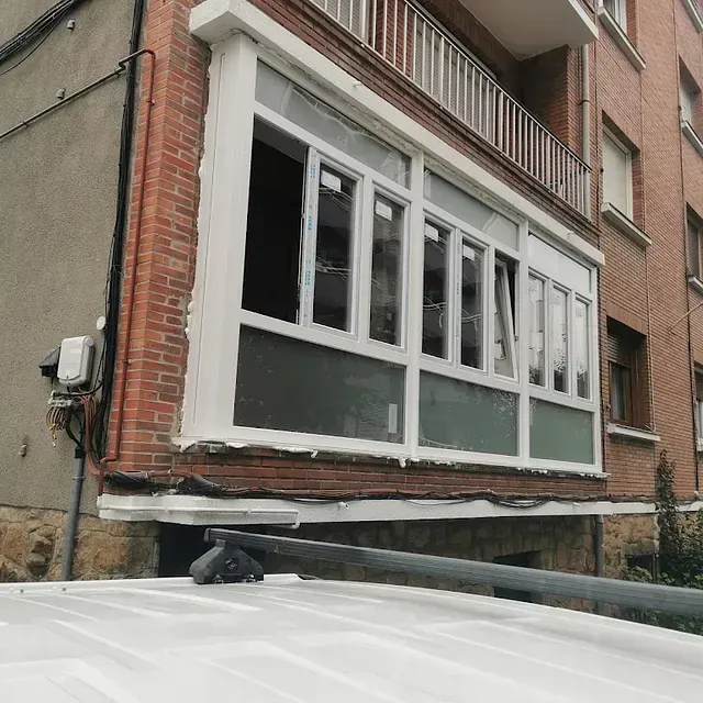 Una furgoneta blanca está estacionada frente a un edificio de ladrillo con balcón.