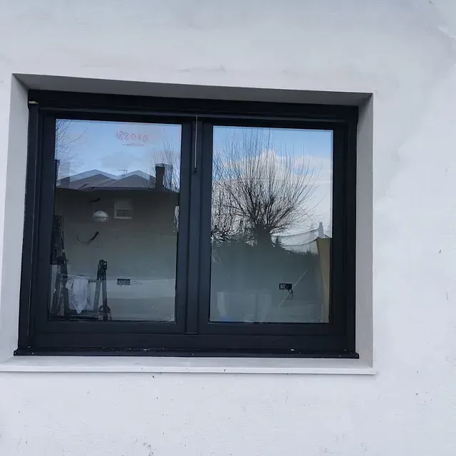 Una ventana negra con un marco blanco está en una pared blanca.