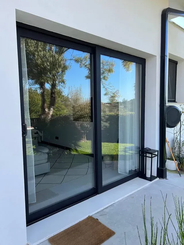 Una puerta corrediza de vidrio se abre a un patio con árboles reflejados en el vidrio.