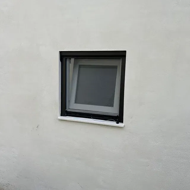Una ventana cuadrada con un marco negro está en una pared blanca.