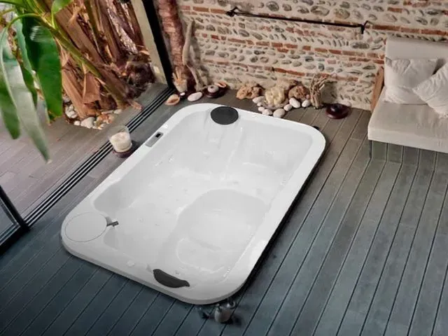Una gran bañera blanca está colocada sobre un suelo de madera en un baño.