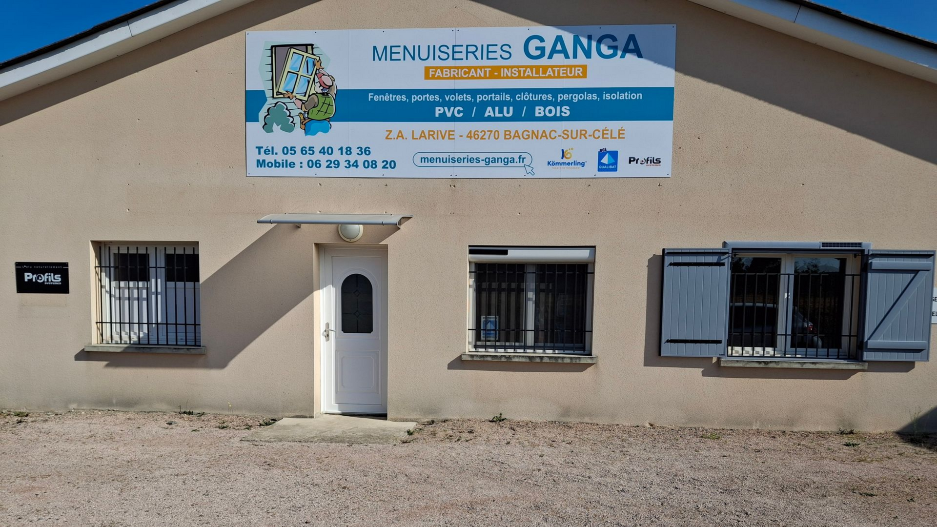 Vitrine de la Menuseries Ganga avec fenêtres, porte et panneau bleu annonçant les services de vitrine.
